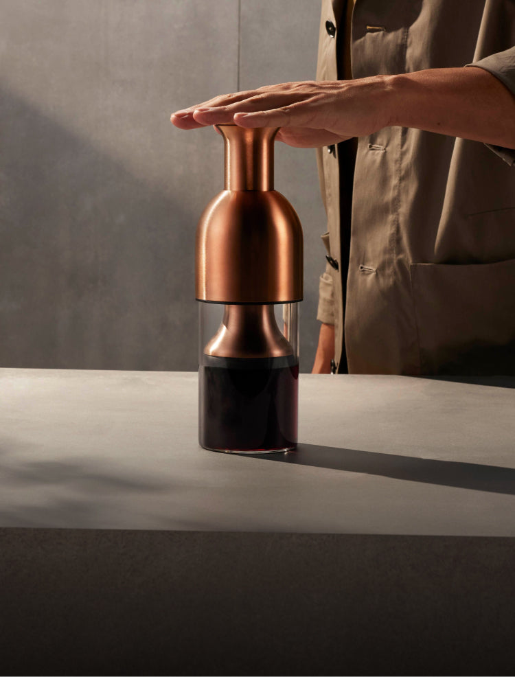 A hand plunging the copper satin eto wine decanter to preserve wine