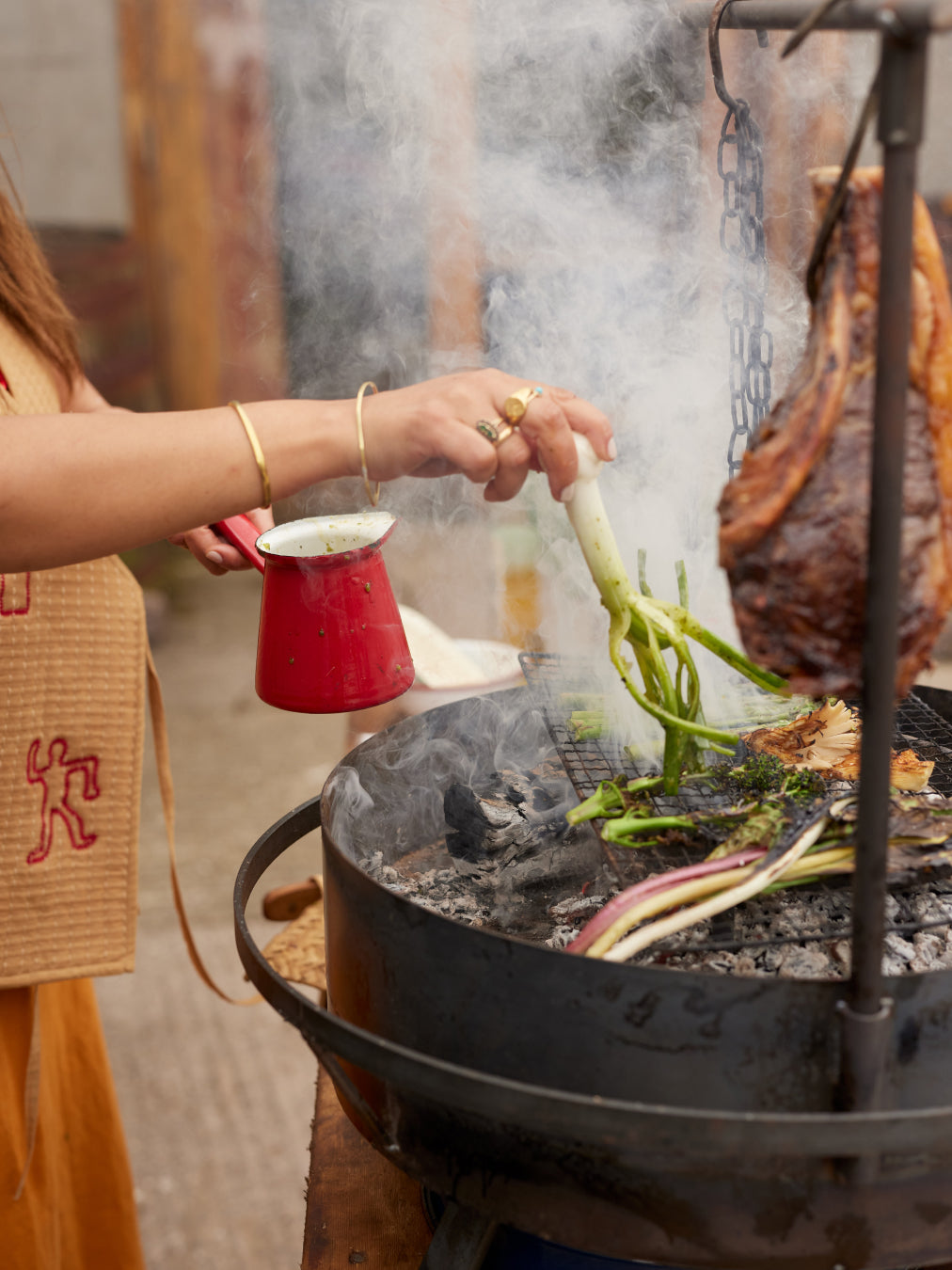 Person cooking food over an open flame with a large pot and vegetables.