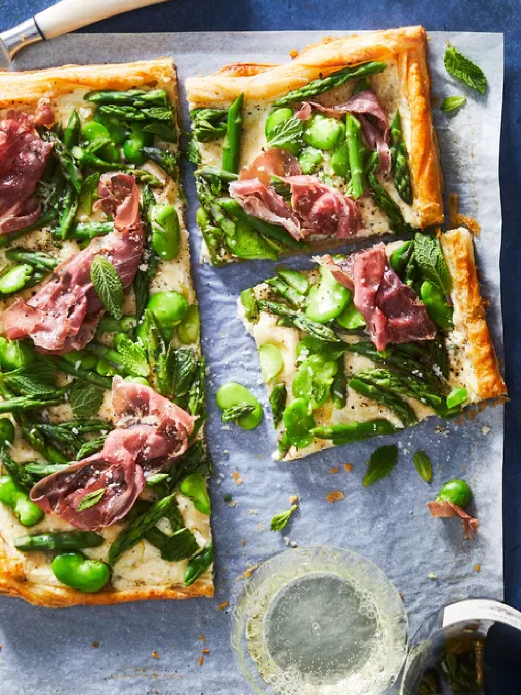 A savoury tart on a slate background with broad beans pancetta and asparagus