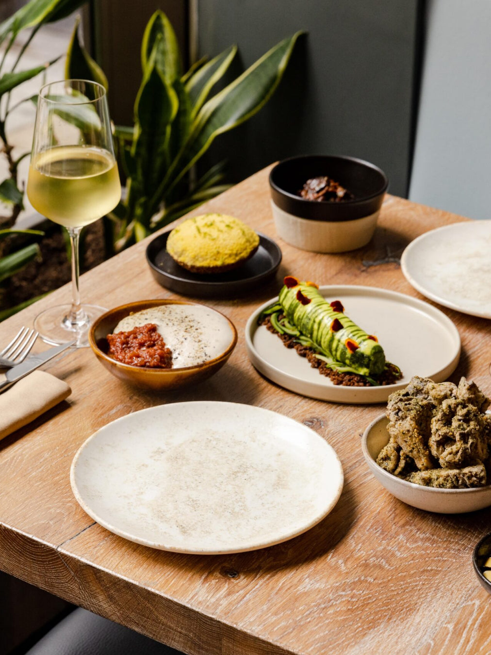 A wooden table with a chilled glass of white wine and several dishes laid out beautifully.