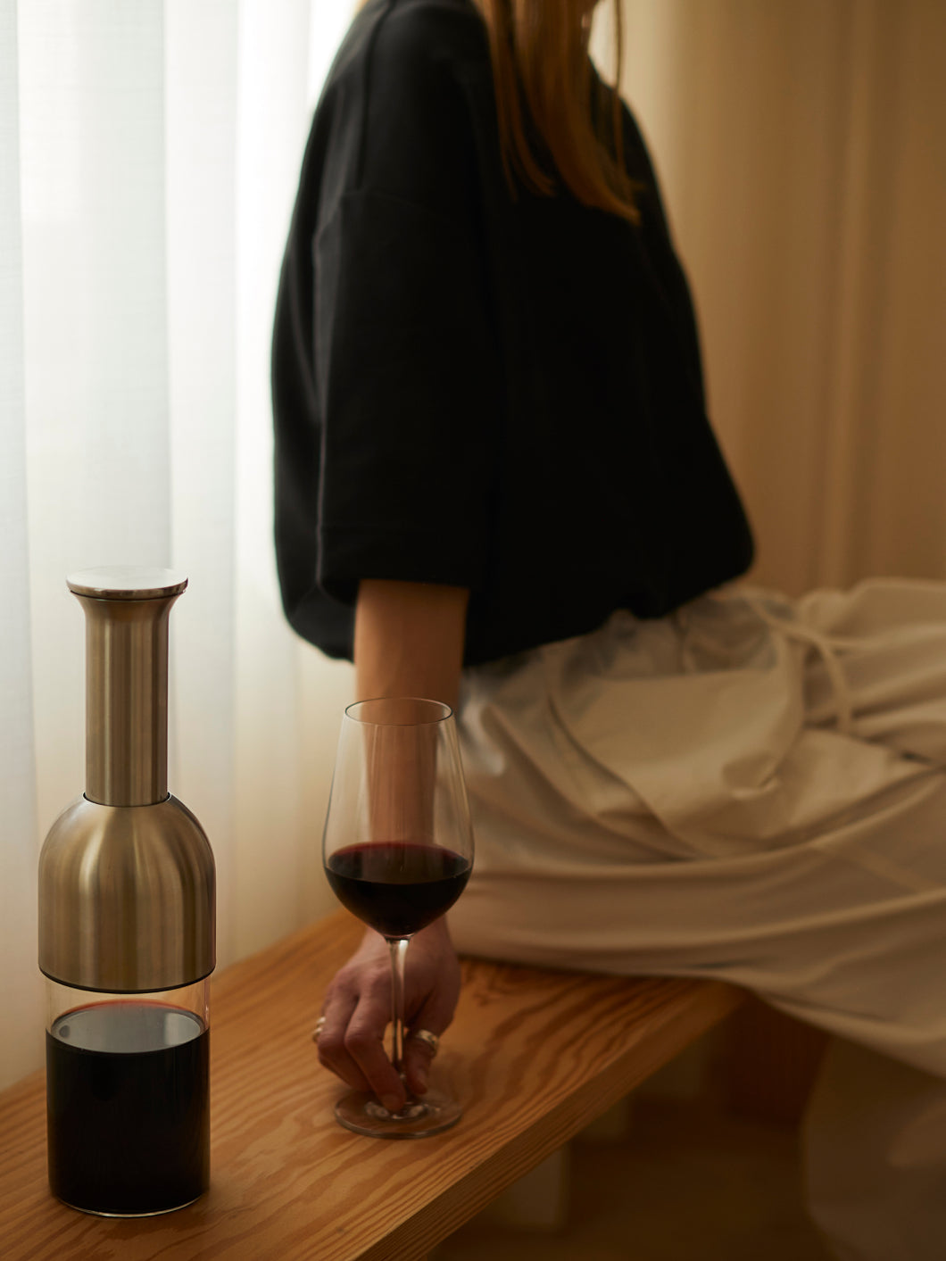 A stainless satin wine decanter beside a woman drinking a glass red wine