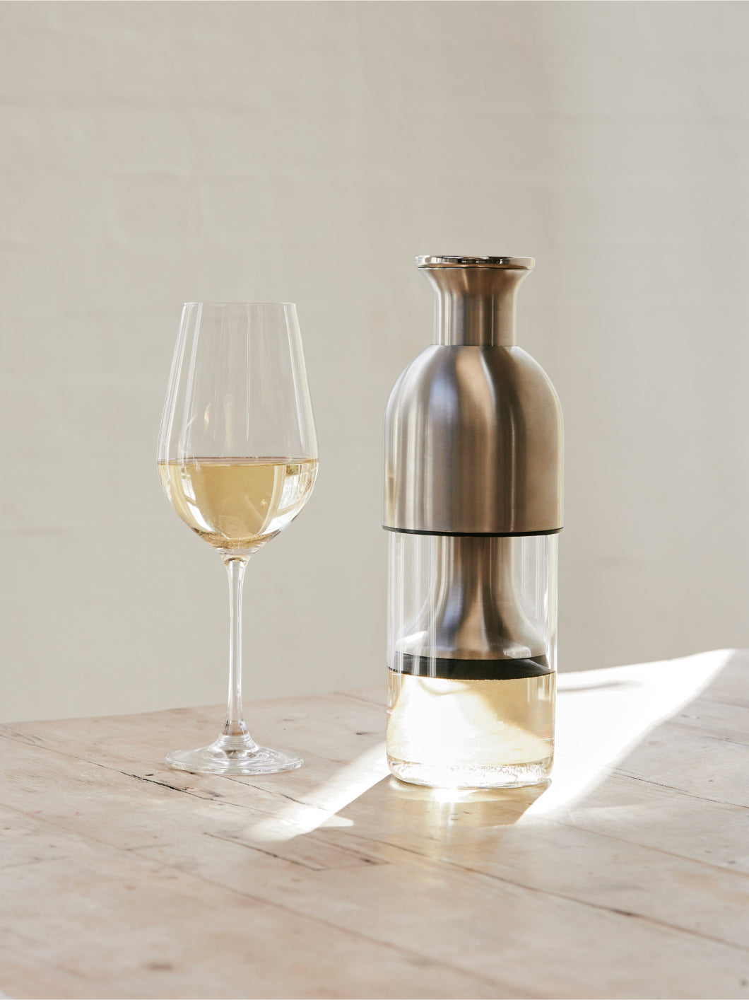 A glass of white wine beside a stainless satin eto wine decanter with white wine in it