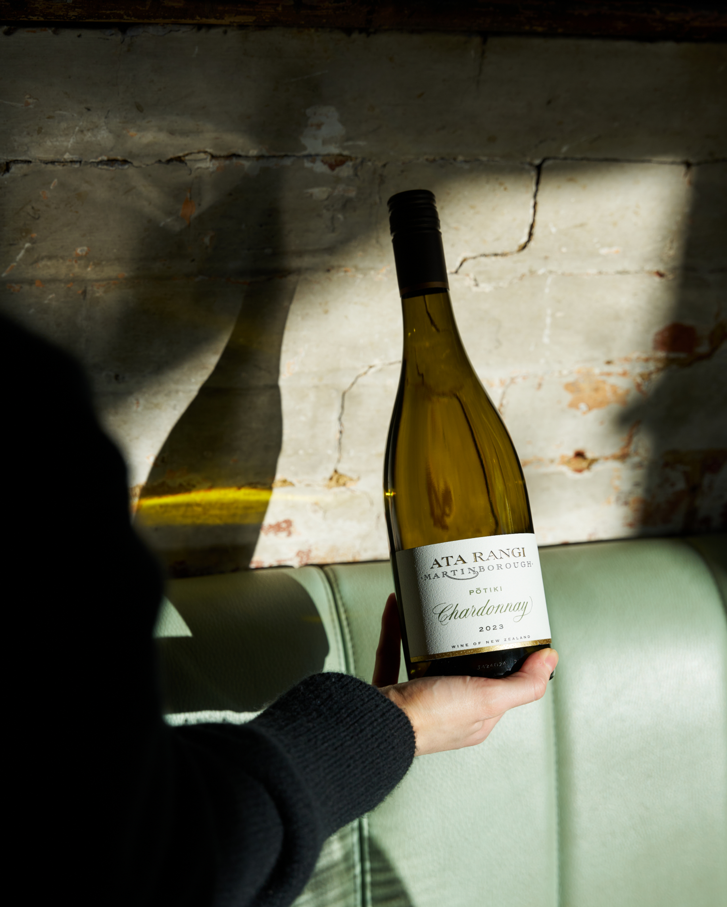 Person holding a bottle of Ata Rangi Chardonnay wine against a textured wall in the Laundry Brixton.