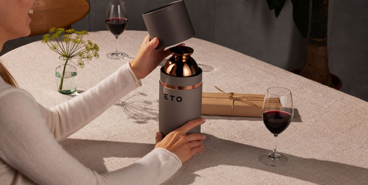 Person using a wine decanter with a glass of red wine on a table.
