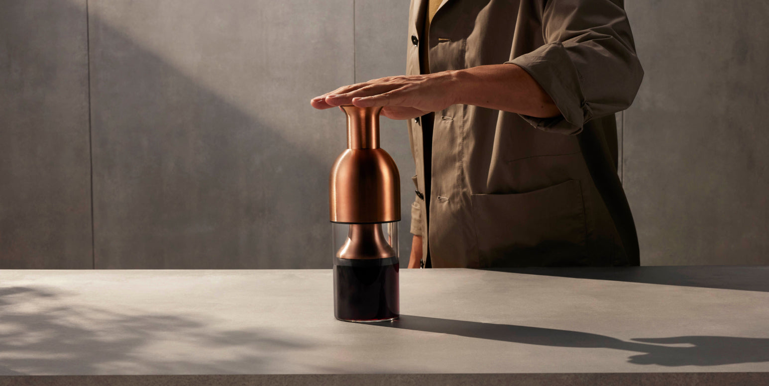 Person holding a copper and glass bottle on a concrete surface with a neutral background