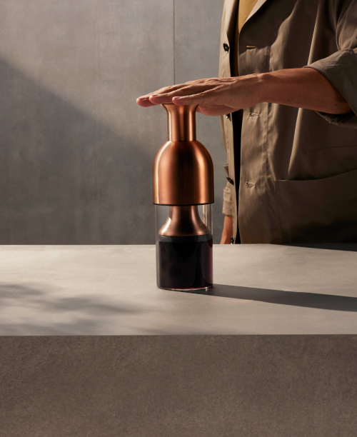 Copper pepper grinder on a gray surface with a person in a beige jacket partially visible.