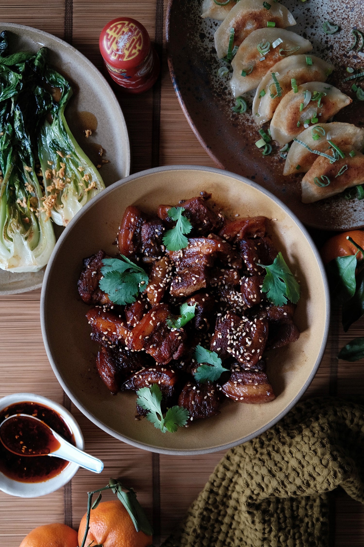 Bowl of pork belly with greens, side dishes on a wooden table