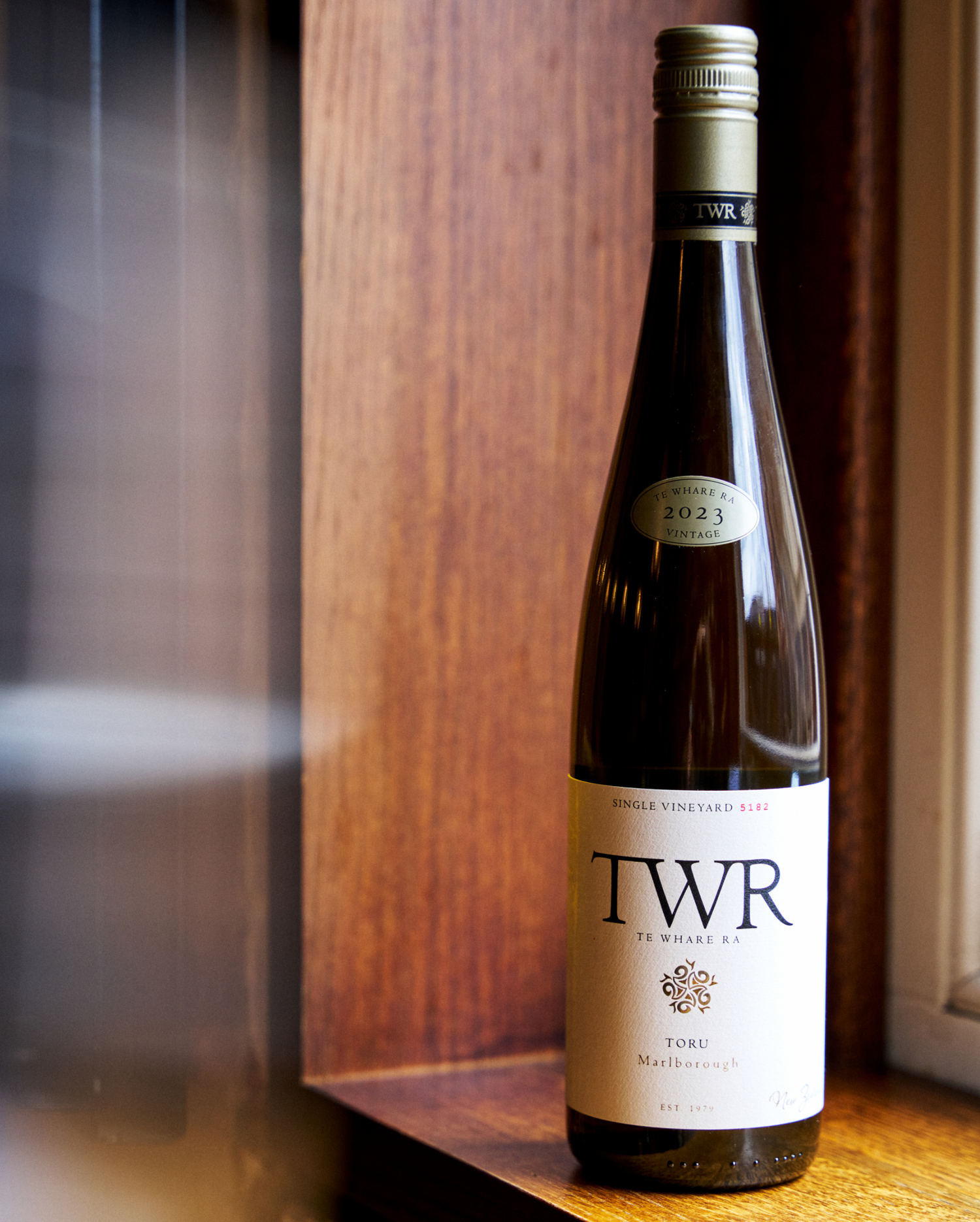 Bottle of Te Whare Ra Toru wine on a wooden surface with a blurred background