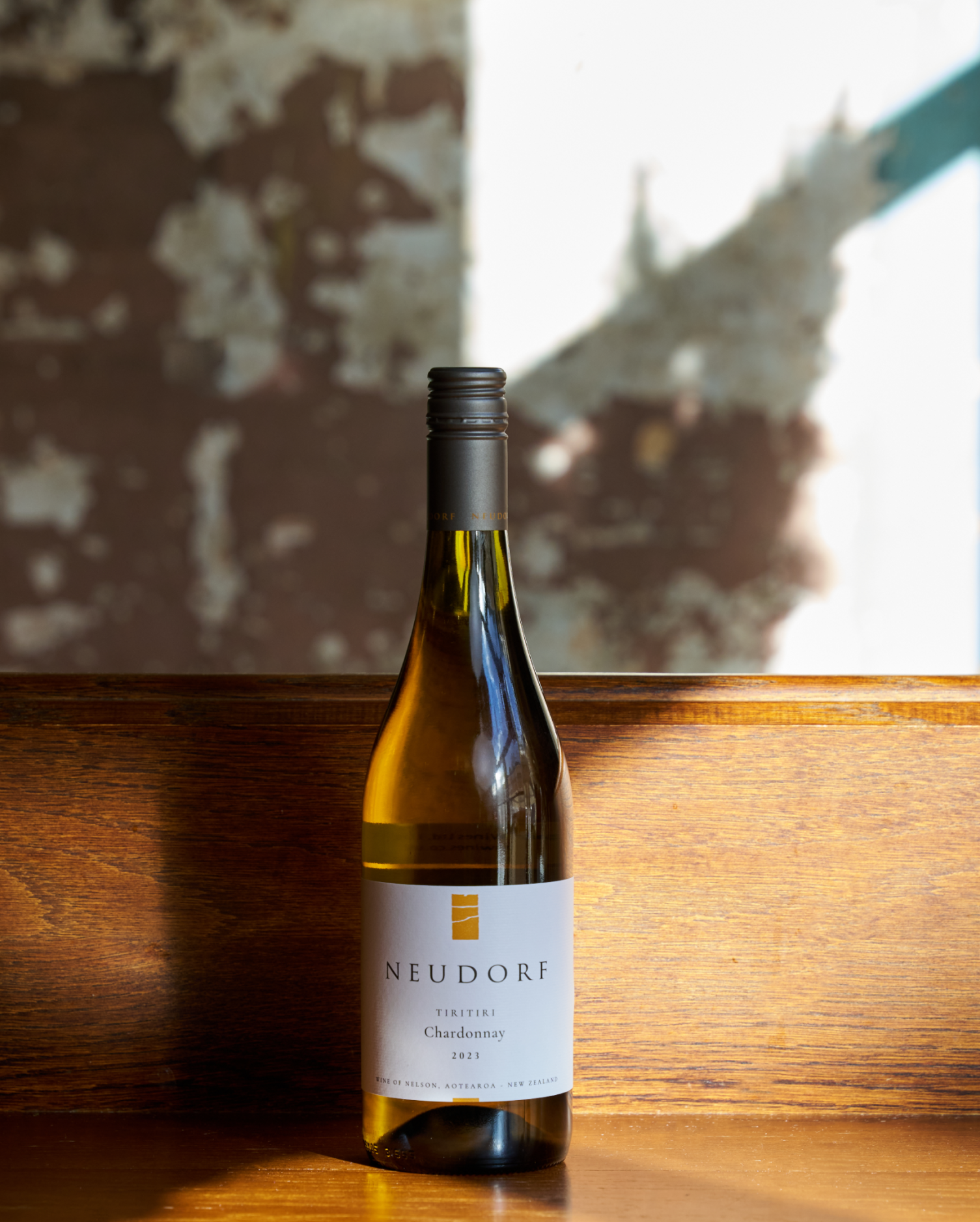 Neudorf Chardonnay wine bottle on a wooden surface with a textured wall in the background