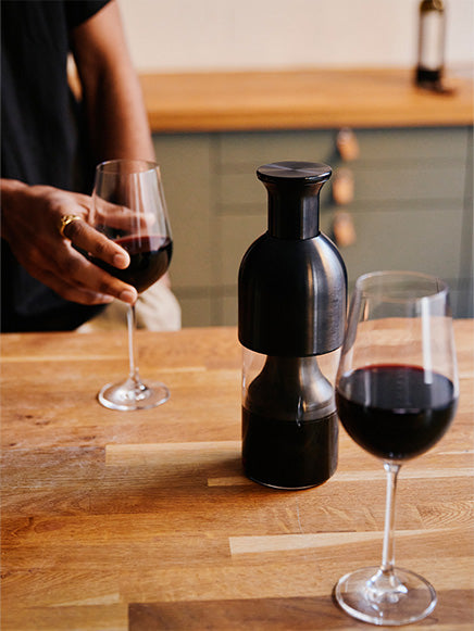 On top of the wooden kitchen counter is a graphite steel eto wine decanter and two red wine glasses