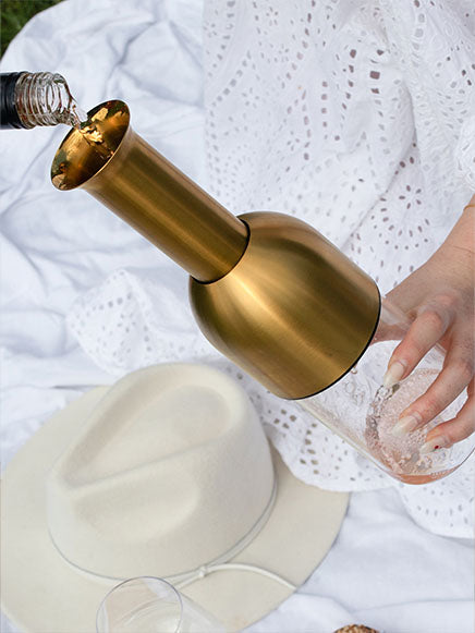 a bottle of rose being decanted into an eto wine preserving decanter in brass satin finish on a picnic day