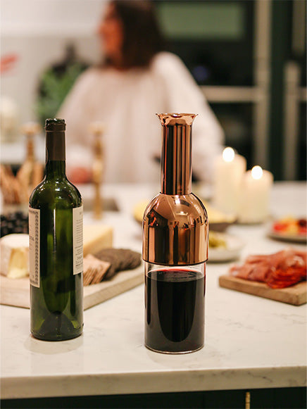 eto wine decanter in copper mirror finish filled with red wine next to a bottle of red wine on the kitchen counter
