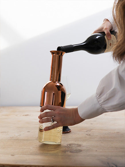 a bottle of white white being decanted into an eto wine decanter in copper mirror finish