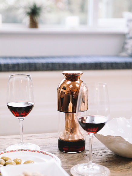 eto wine decanter in copper mirror filled with red wine on top of a wooden table with two glasses of red wine