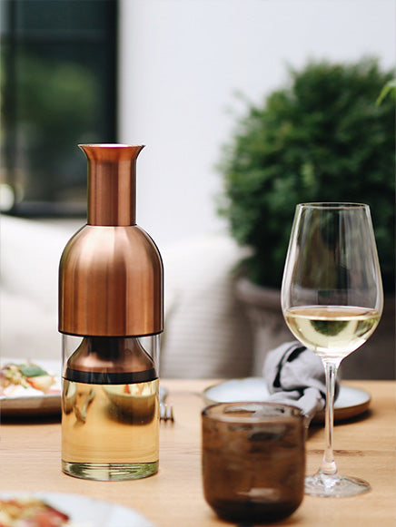 eto wine decanter in brass satin filled with white wine on top of an outdoor dining table