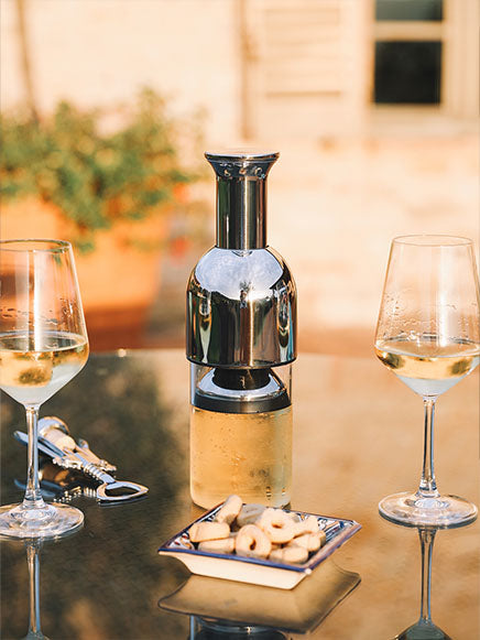 eto wine decanter in stainless steel in between two glasses of white wine on top of a glass table in the garden